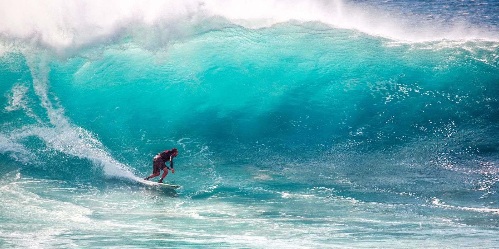 A surfer carving under a breaking wave